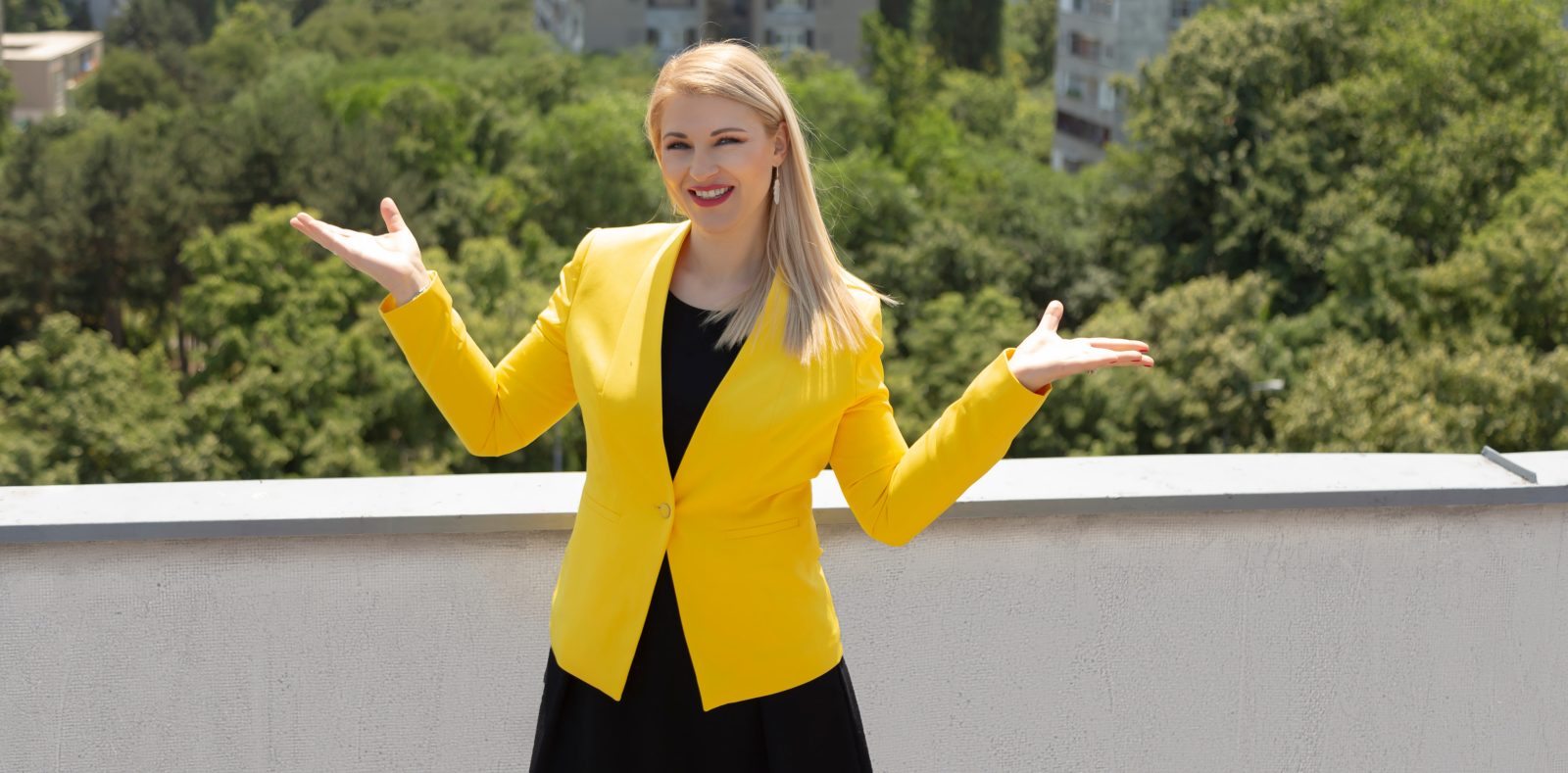 Dr. med. Zorana Pravdić mit offenen Armen im Park, gelber Blazer